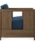 Side view of the Ethnicraft Roan Lounge Chair | Ink, a vintage-inspired chair with a modern, boxy wooden frame and dark blue upholstered seat and back cushions. The design features a rectangular cutout in the wooden side panel.