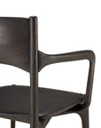 A close-up of Ethnicraft's PI Dining Chair - Teak Dark Brown with arms, highlighting its curved backrest, angled armrests, and contoured seat—modern handcrafted furniture displayed against a white background.