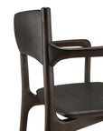 A close-up of the Ethnicraft PI Dining Chair – Teak Dark Brown with arms, highlighting its curved backrest, armrest, and seat crafted from dark wood, set against a white background.