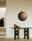 An Ethnicraft Flow Console | Mahogany Rose Brown with cut-out legs stands against a wall beneath a large circular mirror with a gradient finish.