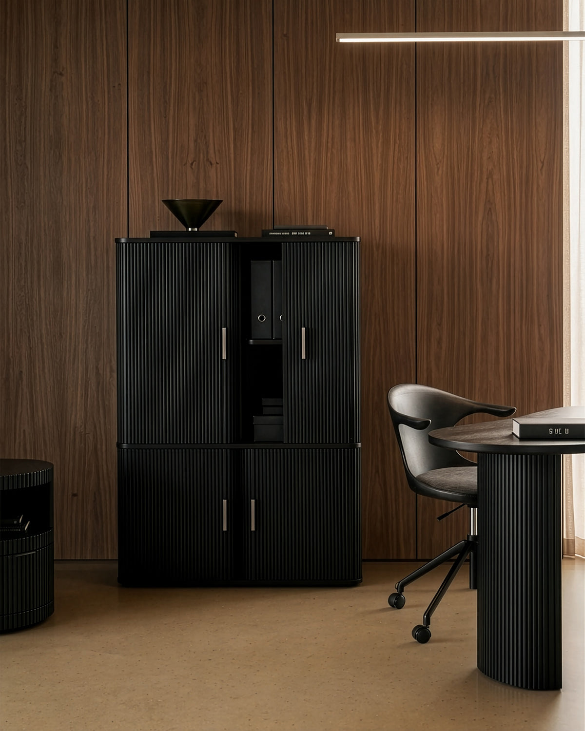 Modern office with wood-paneled walls, an Ethnicraft Roller Max Filing Cabinet in black, a matching black desk, a swivel chair, and minimal décor, including a black bowl and a sleek linear light for stylish and functional storage.