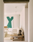 A minimal living room features a beige sectional sofa, wooden coffee table, black lamp, décor pieces, and a large green and white abstract painting above a wooden chair and the Ethnicraft Kabuki Side Table - Oak.