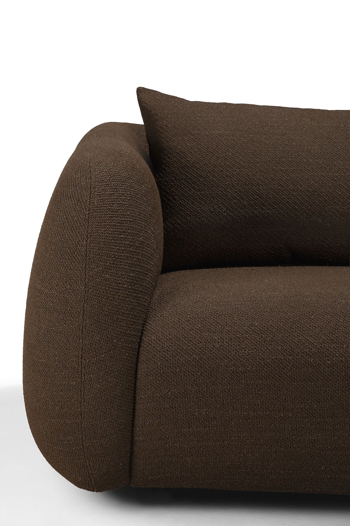 Close-up of a modern, dark brown upholstered Ethnicraft Figur Sofa | 3 Seater with rounded armrest and a matching cushion, set against a white background—an ideal statement piece for contemporary living.