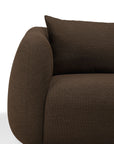 Close-up of a modern, dark brown upholstered Ethnicraft Figur Sofa | 3 Seater with rounded armrest and a matching cushion, set against a white background—an ideal statement piece for contemporary living.