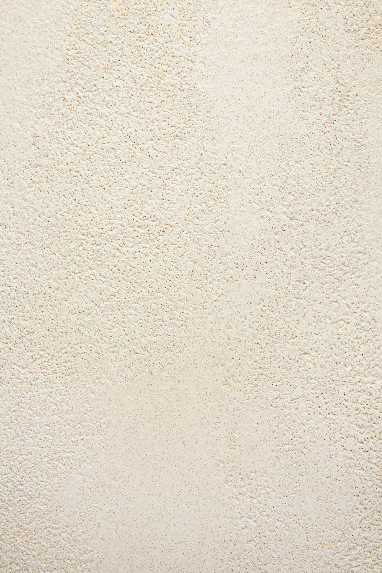 A close-up of a textured off-white wall with small bumps and rough patches, ideal as a backdrop for the Ethnicraft Blend Dining Table - Microcement with interchangeable tops. Even lighting enhances the wall’s unique texture.