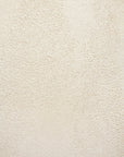 A close-up of a textured off-white wall with small bumps and rough patches, ideal as a backdrop for the Ethnicraft Blend Dining Table - Microcement with interchangeable tops. Even lighting enhances the wall’s unique texture.