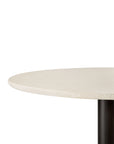 A close-up shows the smooth, light-toned microcement tabletop of the Ethnicraft Blend Dining Table, featuring its round surface and a dark cylindrical base against a white background.
