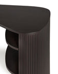 A close-up of the Ethnicraft Roller Max Desk shows its dark mahogany corner, rounded triangular top, vertical grooved side panel, and two curved shelves beneath, all set against a white background.