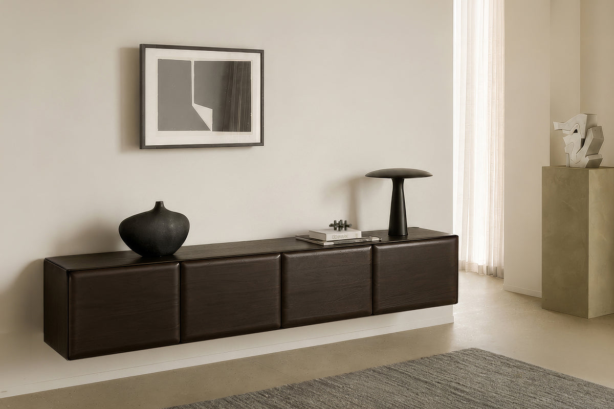 A wall-mounted Ethnicraft PI Light Hanging Sideboard in dark wood with four cabinet doors, topped with a vase, a book, and a lamp.