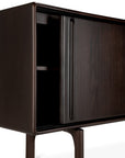 A close-up of the Ethnicraft Flow Sideboard shows its modern dark wood design with rounded edges, slim legs, and an open sliding door revealing partially visible interior shelves, set against a white background.