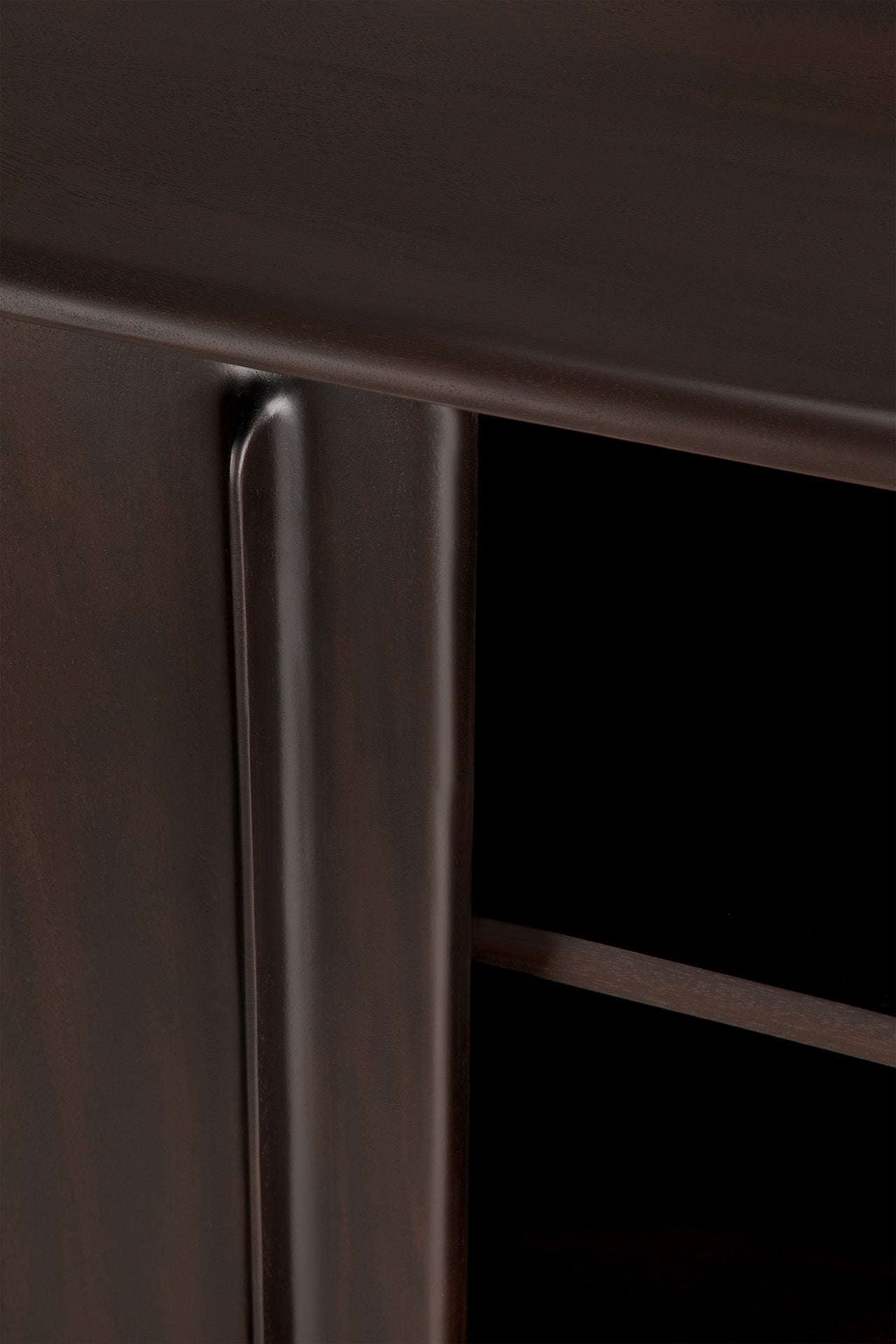 Close-up of the Flow Sideboard by Ethnicraft in dark brown mahogany, highlighting a smooth corner edge, part of the door, and interior shelf. The polished surface emphasizes its vintage modern design and refined craftsmanship.