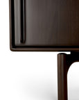 Close-up of the Flow Sideboard by Ethnicraft, featuring a dark wood finish, a vertical handle on the door, and a rounded leg beneath, set against a white background.