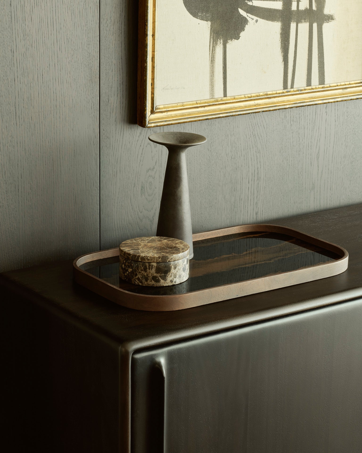 A minimal decor setup featuring a rectangular wooden tray, round marble box, and matte ceramic vase arranged on the Ethnicraft Flow Sideboard, with a modern abstract painting displayed above.