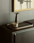 A minimal decor setup featuring a rectangular wooden tray, round marble box, and matte ceramic vase arranged on the Ethnicraft Flow Sideboard, with a modern abstract painting displayed above.