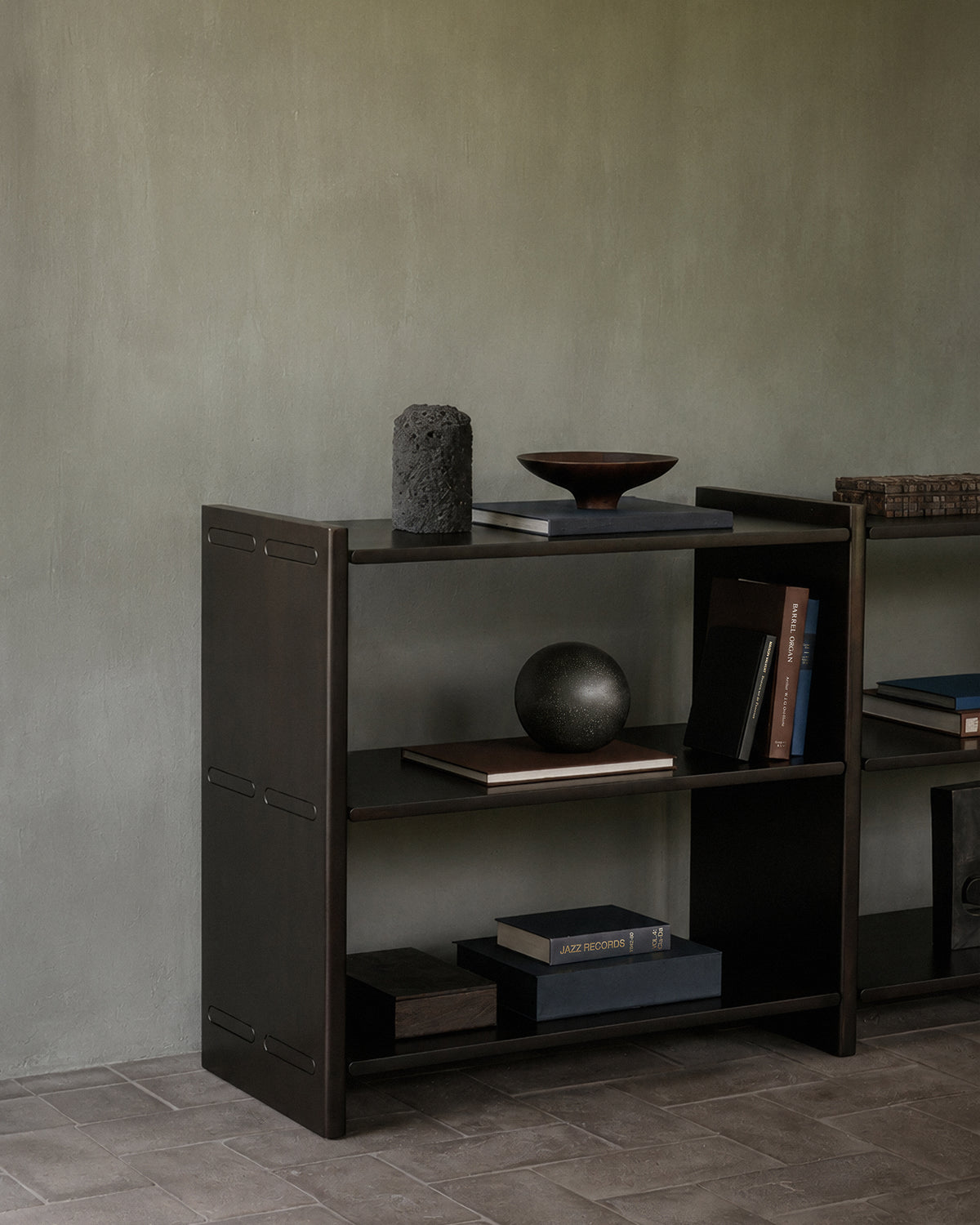 A low, dark mahogany Mortise Rack holding books, a bowl, and decorative objects.