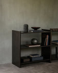 A low, dark mahogany Mortise Rack holding books, a bowl, and decorative objects.