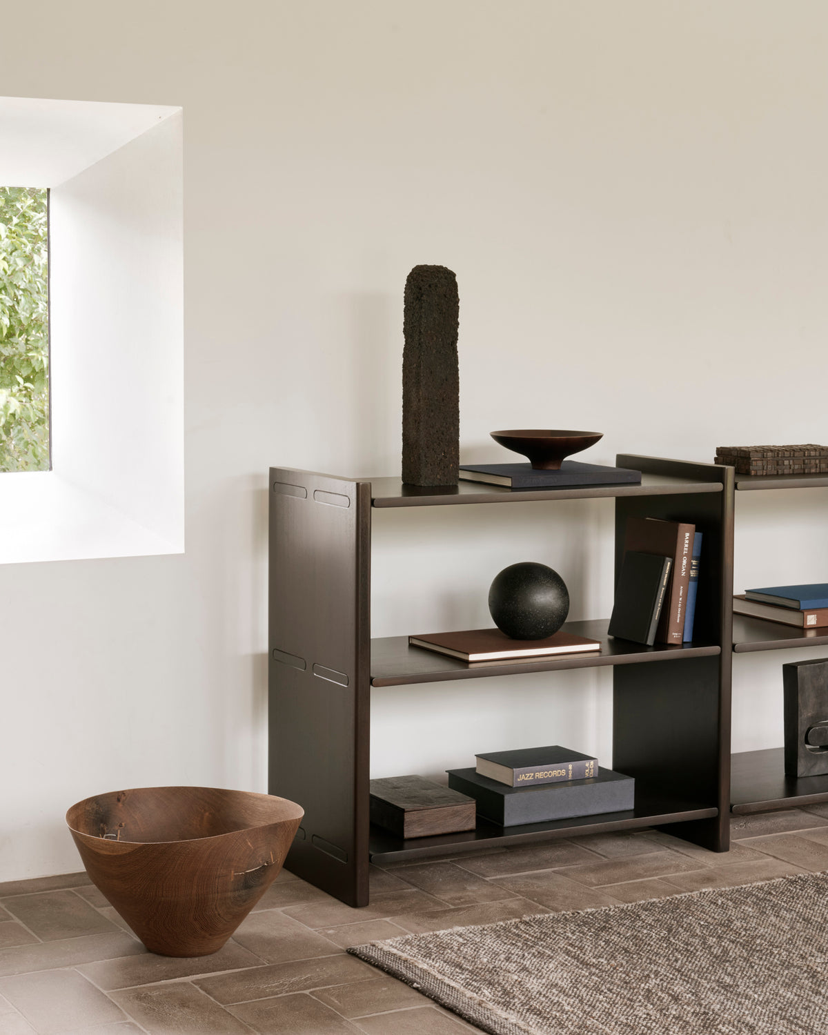 Two heirloom-quality mahogany Mortise Rack units hold decorative objects and books, with a large wooden bowl placed on the floor in the foreground.