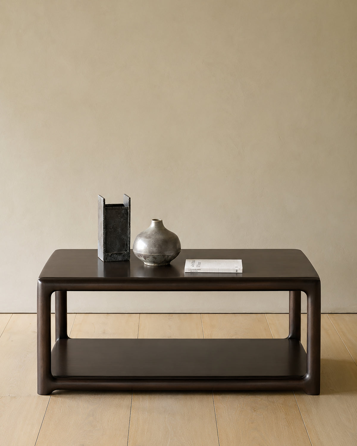 A dark wood Ethnicraft Eda Coffee Table | Square with a lower shelf, topped with a rectangular vase, a round vase, and a book.