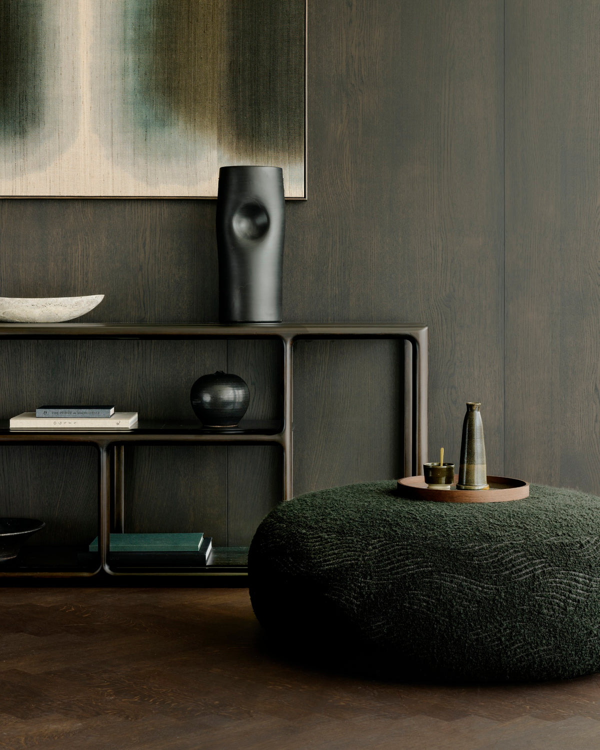 Wide, heirloom-quality Eda Console | Wide by Ethnicraft in dark wood with open shelving holding books and decorative objects, placed against a dark paneled wall.