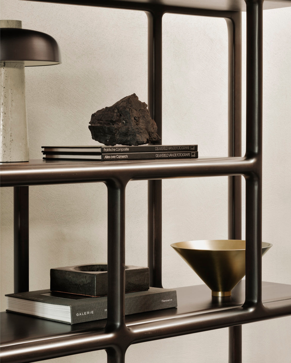 A dark wood Ethnicraft Eda rack holds books, a lamp, a rock, a square container, and a metallic bowl.