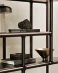 A dark wood Ethnicraft Eda rack holds books, a lamp, a rock, a square container, and a metallic bowl.