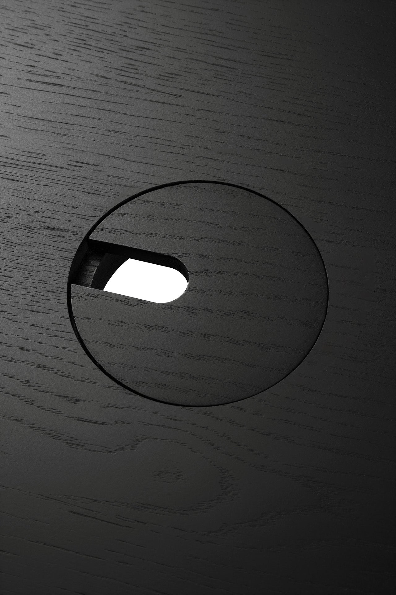 Close-up of Ethnicraft’s U Desk - Black Oak, showing its distinct wood grain, black oak finish, circular cutout, and oval slot contrasted against a white background.