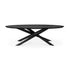 The Ethnicraft Mikado Dining Table Oval in Black Oak features a modern flat top with four angled, intersecting legs forming a sculptural geometric base, shown against a white background.