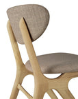 A close-up side view of the Ethnicraft Eye Dining Chair – Oak with Warm Grey Fabric highlights its solid oak frame, curved upholstered seat and backrest, smooth rounded edges, and elegant minimalist design.