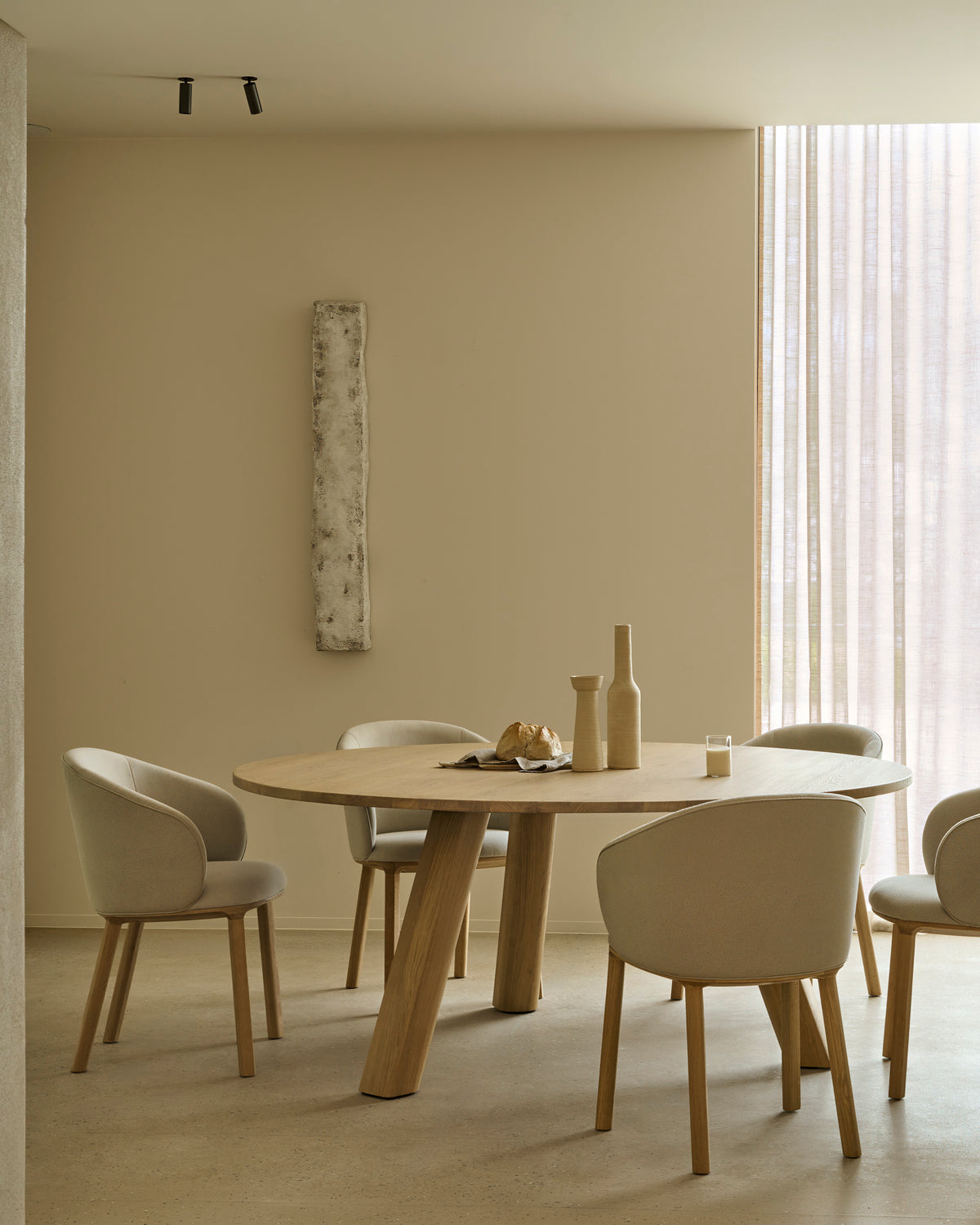 A round solid oak Unda Dining Table surrounded by four upholstered chairs with light-colored fabric.