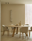 A round solid oak Unda Dining Table surrounded by four upholstered chairs with light-colored fabric.