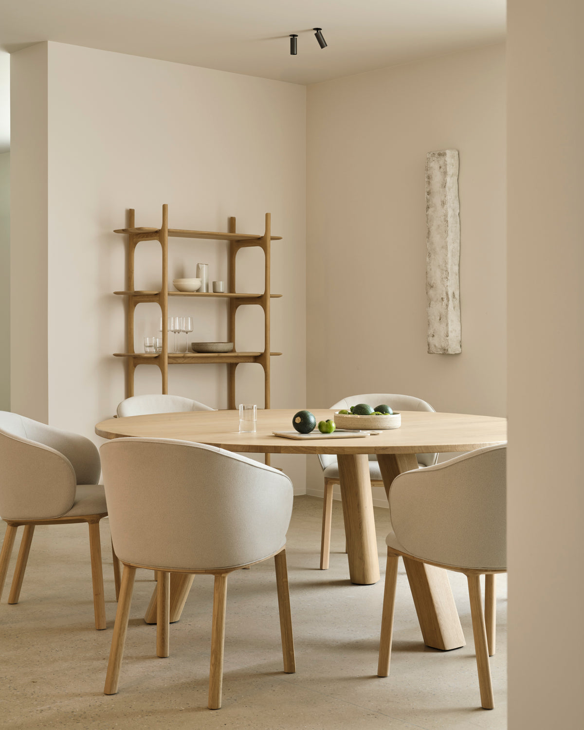 Round solid oak Unda Dining Table by Ethnicraft with four upholstered chairs, set in a room with a wooden shelving unit.