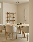 Round solid oak Unda Dining Table by Ethnicraft with four upholstered chairs, set in a room with a wooden shelving unit.