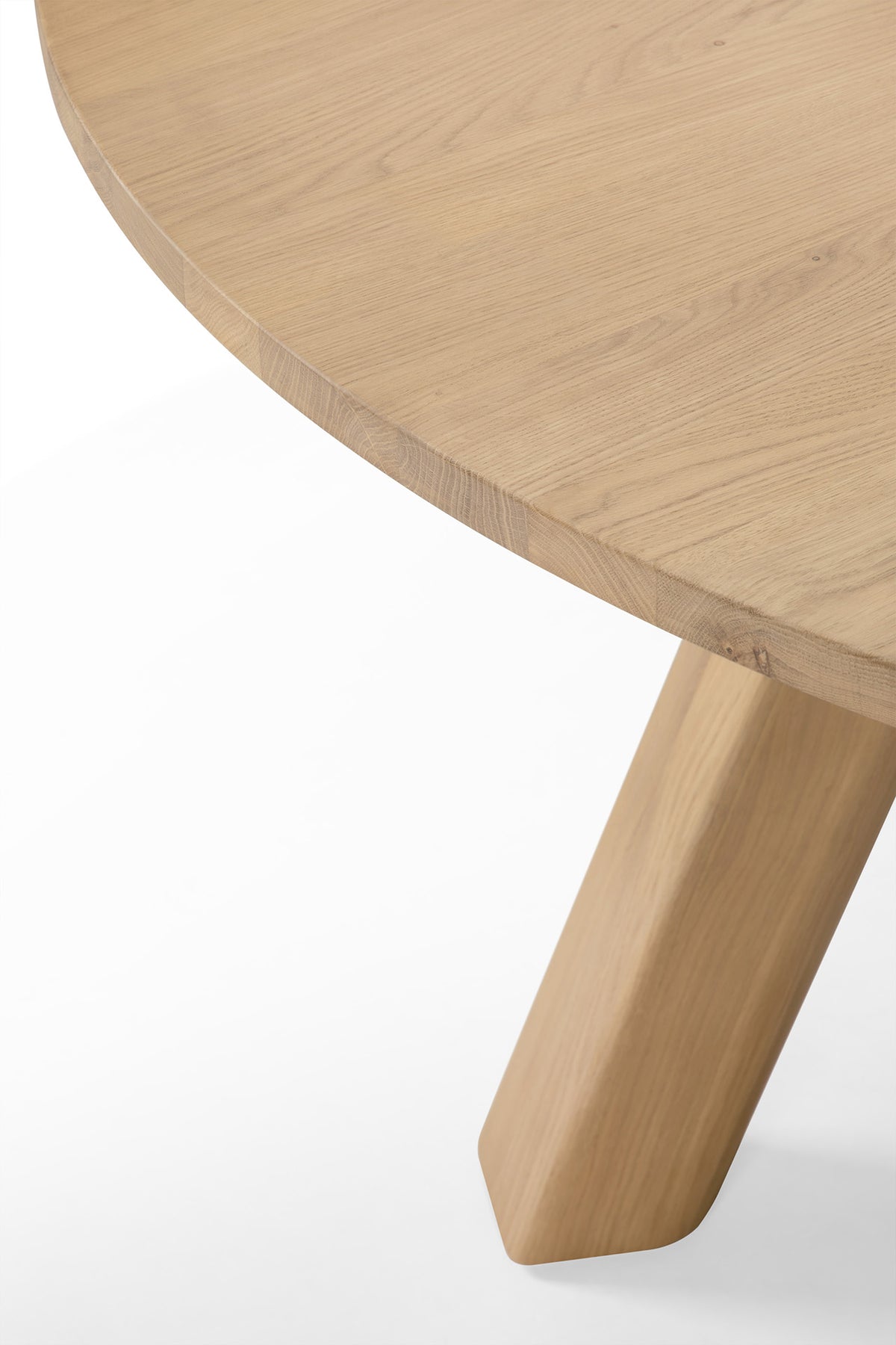 Close-up of a circular solid oak Unda Dining Table by Ethnicraft, featuring a thick, angled leg.