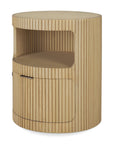 The Boomerang Drawer Unit - Oak by Ethnicraft is a round, light solid oak nightstand featuring vertical grooves, an open middle shelf, and a lower cabinet door with a small black handle.