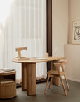Minimalist home office with an Ethnicraft light wood desk and chair, Ethnicraft Boomerang Drawer Unit – Oak, notepad, book, sculptural lamp, water bottle, sheer curtains filtering light, and a Picasso print on the beige wall.