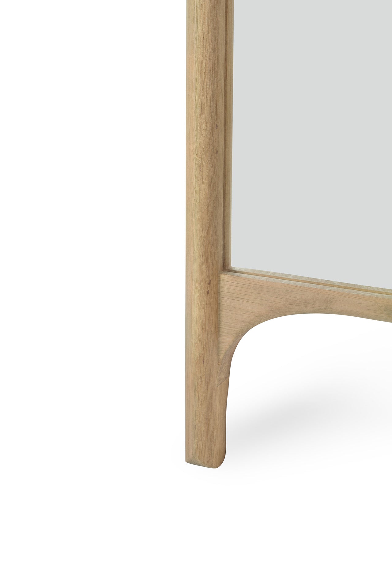 A close-up of the Ethnicraft PI Floor Mirror - Oak captures the smooth, light oak wood with curved detailing, a polished yet imperfect finish at the bottom corner, and part of the reflective glass.