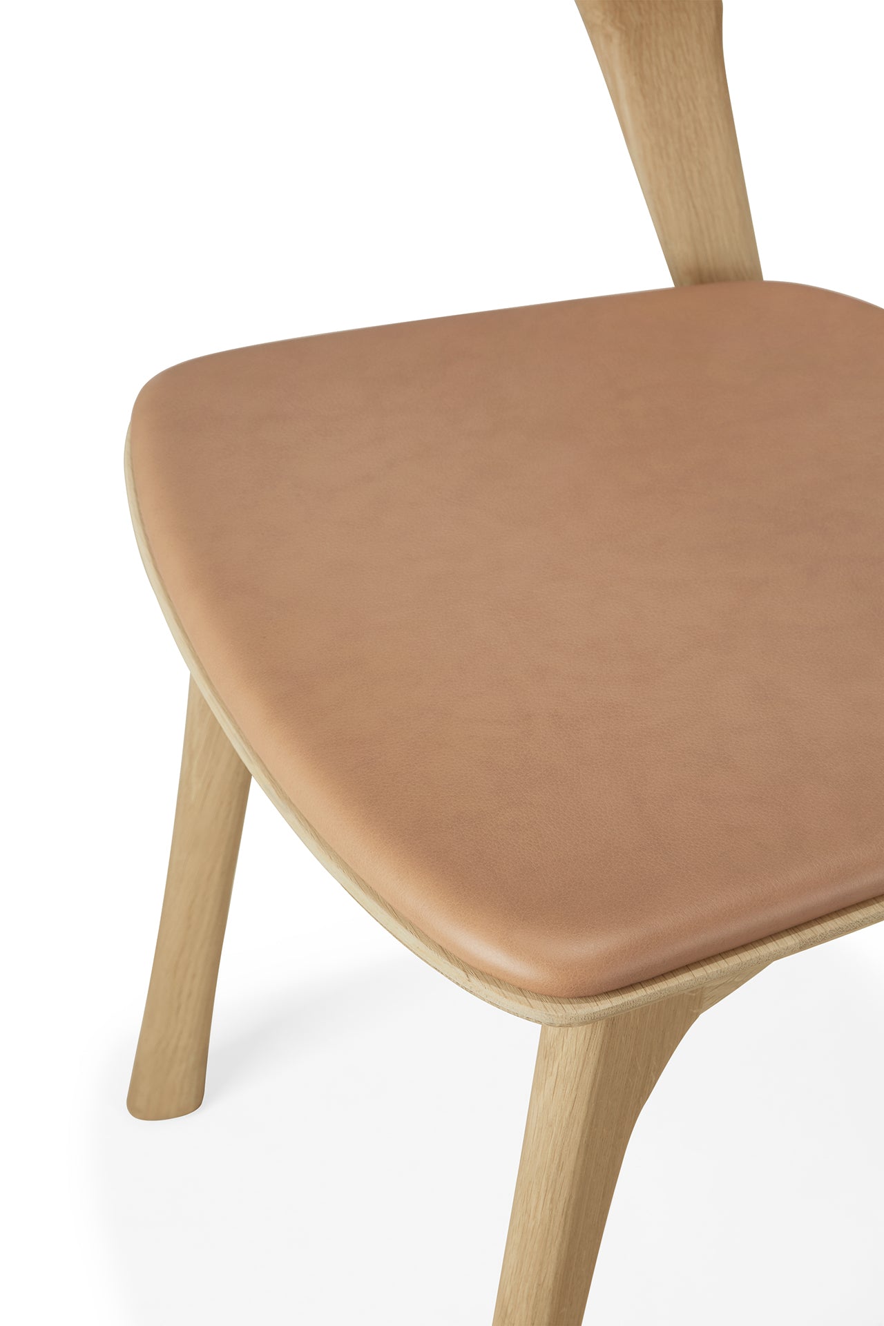 A close-up of the Ethnicraft Bok Dining Chair, made from solid oak with light wood legs and a sienna leather seat cushion, photographed against a white background.