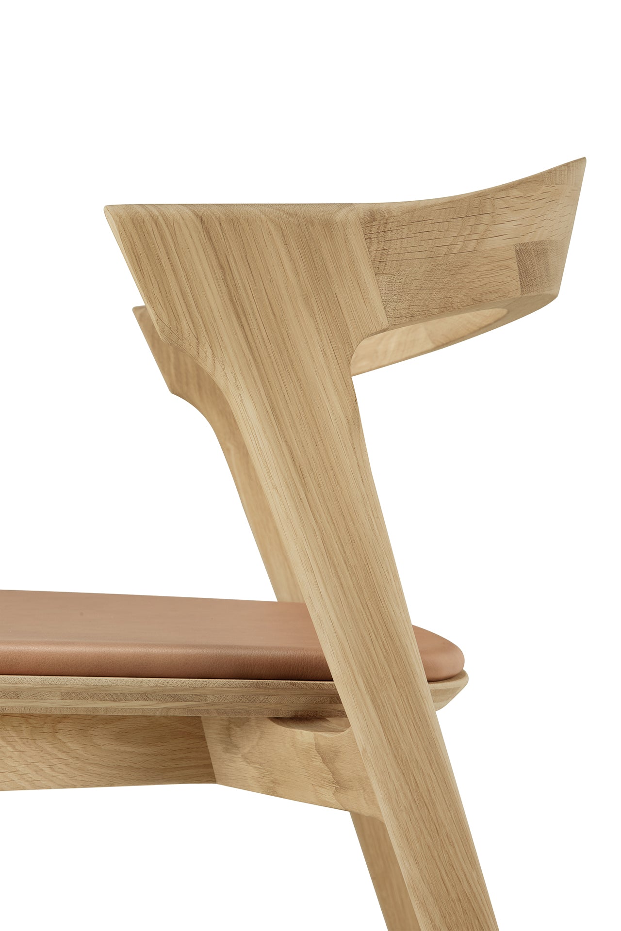 A close-up side view of the Ethnicraft Bok Dining Chair in solid oak with a sienna leather seat, showcasing its curved backrest, minimalist design, and elegant European oak wood grain.