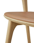 Close-up of the Ethnicraft Bok Dining Chair, crafted from solid oak with light-colored legs and a Sienna leather upholstered seat, shown against a white background.