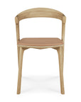 The Bok Dining Chair by Ethnicraft, made from solid oak with a curved backrest and a sienna leather cushioned seat, is shown from the front against a white background.