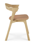 Side view of the Ethnicraft Bok Dining Chair, crafted from solid oak with a curved backrest and sienna leather seat. The chair boasts clean, minimalist lines and a natural wood finish.
