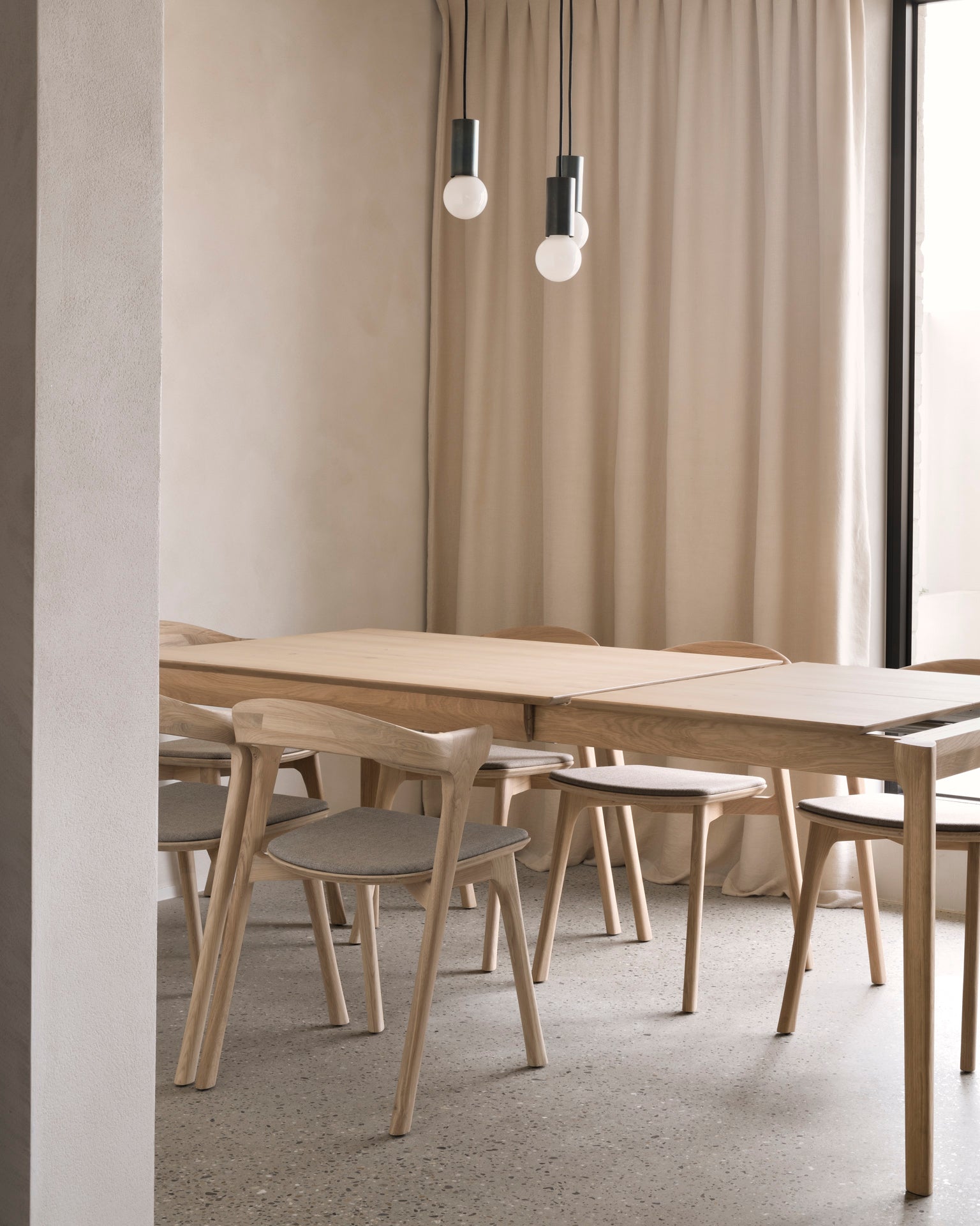 The Ethnicraft Bok Extendable Dining Table in Varnished Oak, paired with chairs, creates a stylish centerpiece for any dining room.