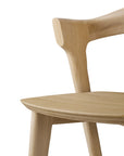 Close-up of an Ethnicraft Bok counter stool, crafted from solid oak, highlighting its smooth natural finish, angled backrest, and curved seat against a white background.