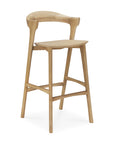 The Bok bar stool by Ethnicraft is crafted from solid oak with a light wood finish, featuring a minimalist design, curved low backrest, four legs with support bars, and a flat rectangular seat inspired by the Bok dining chair.