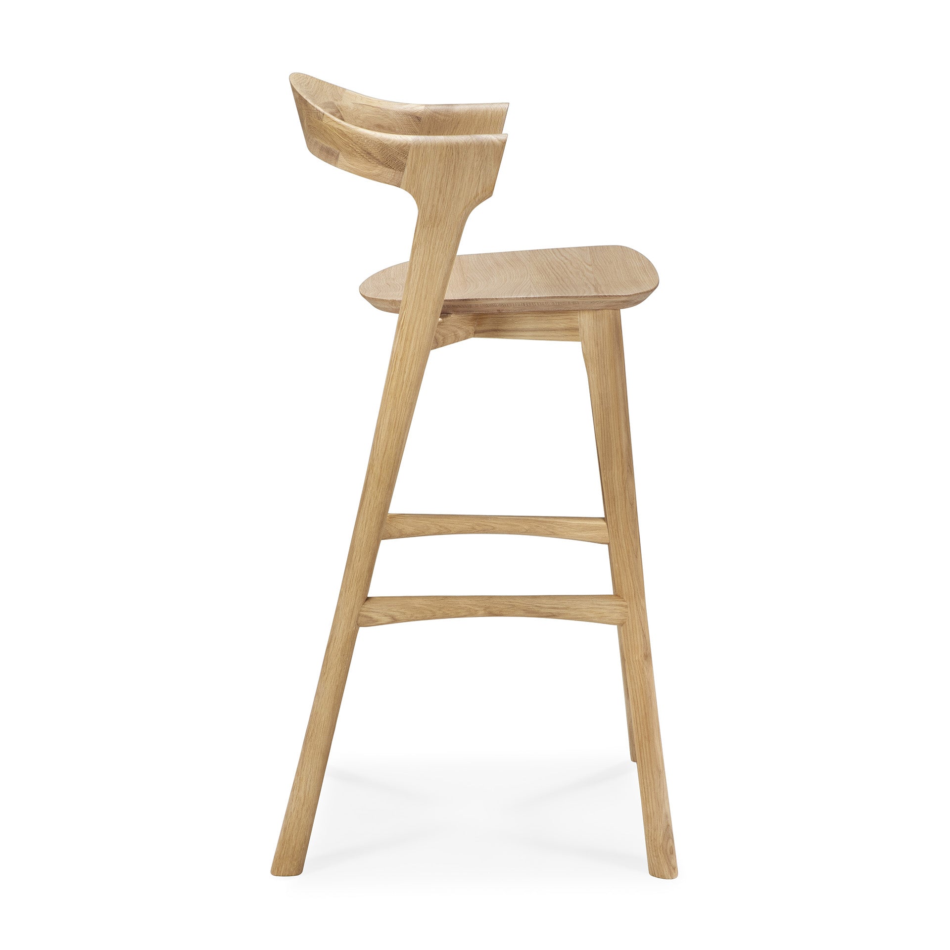 Side view of the Ethnicraft Bok bar stool - Oak, featuring a curved backrest, gently angled legs, a footrest, and a natural solid oak finish.
