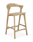 The Ethnicraft Bok counter stool is a minimalist wooden bar stool with a curved backrest, no armrests, and a natural solid oak finish, inspired by the design of the Bok dining chair.