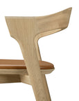 Side view of the Ethnicraft Bok bar stool in solid oak, featuring a curved backrest and brown cushioned seat with clean lines and minimalist design, set against a white background.