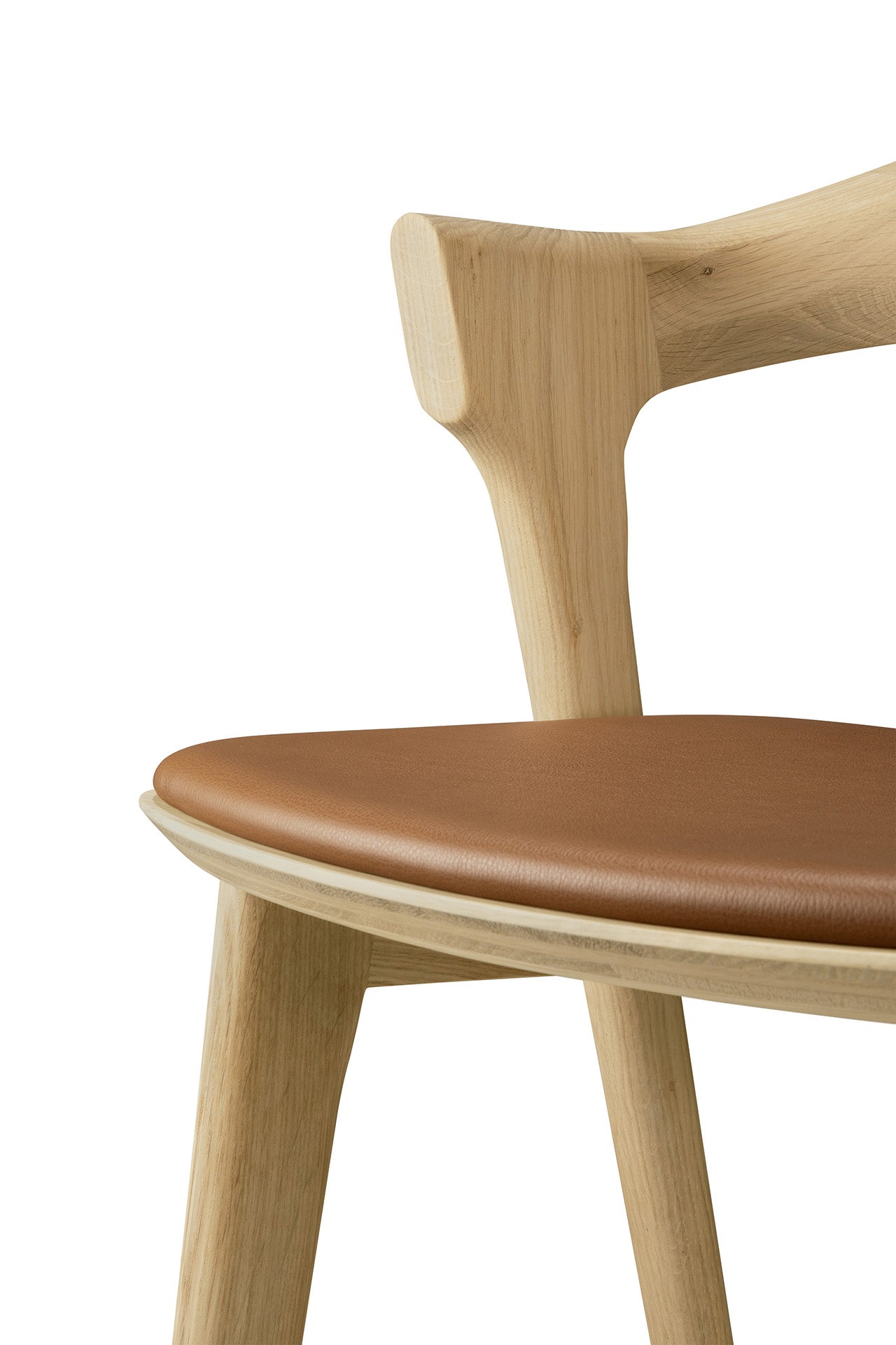 A close-up of the Ethnicraft Bok bar stool in solid oak, featuring a curved backrest and a brown leather seat cushion, shown against a white background.