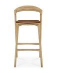 The Ethnicraft Bok bar stool in solid oak features a curved backrest and a brown cushioned seat, shown from the front on a white background.