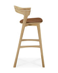 Side view of the Ethnicraft Bok bar stool in solid oak with a curved backrest and brown cushioned seat, set against a white background.